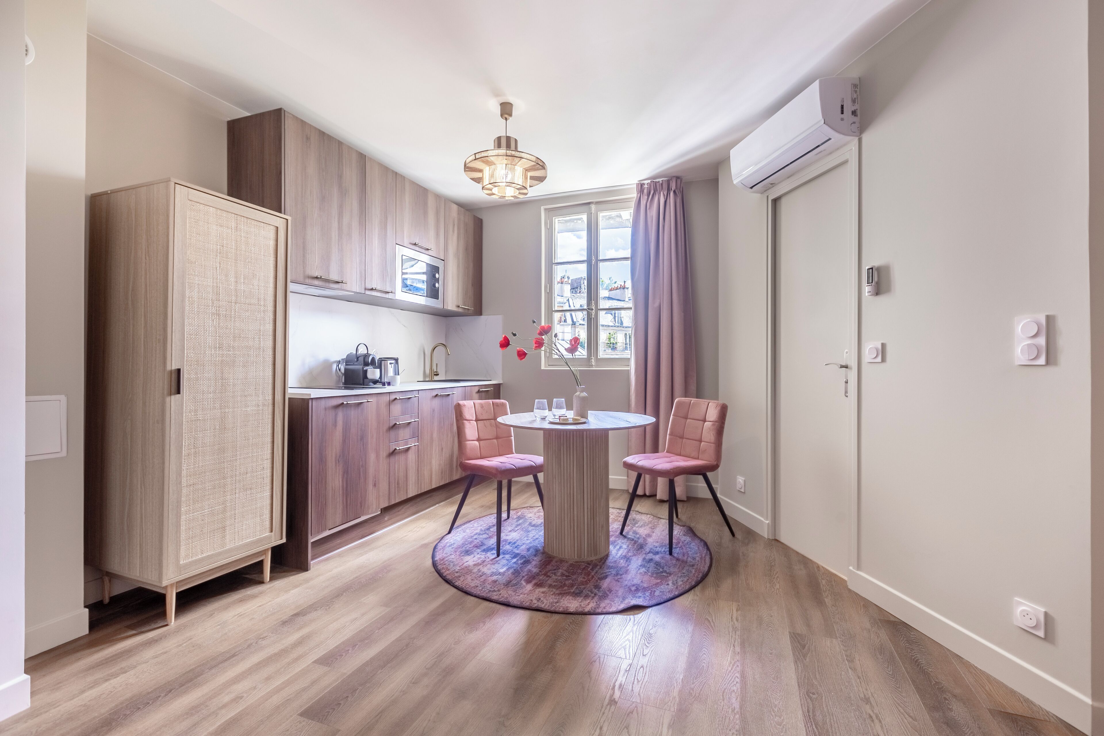 A modern kitchen with wooden cabinets, a dining table with chairs, and a central light fixture.