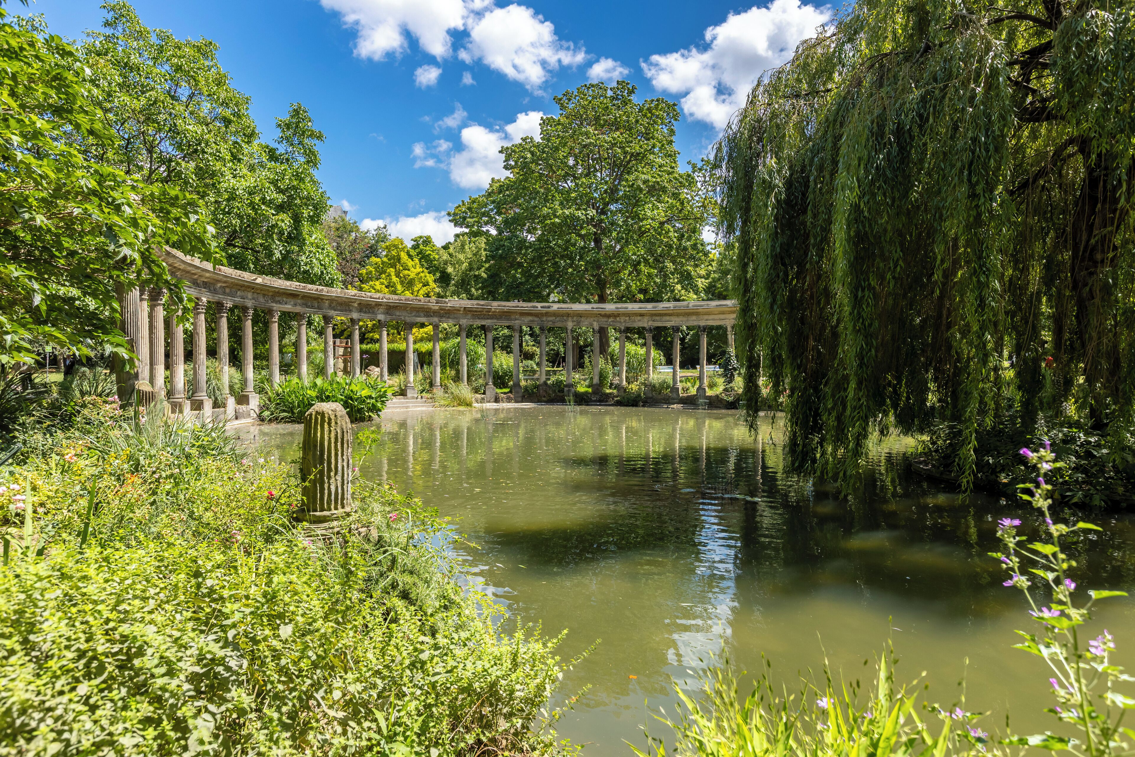 Een rustige tuin met een klassiek paviljoen, een vijver en weelderige begroeiing.