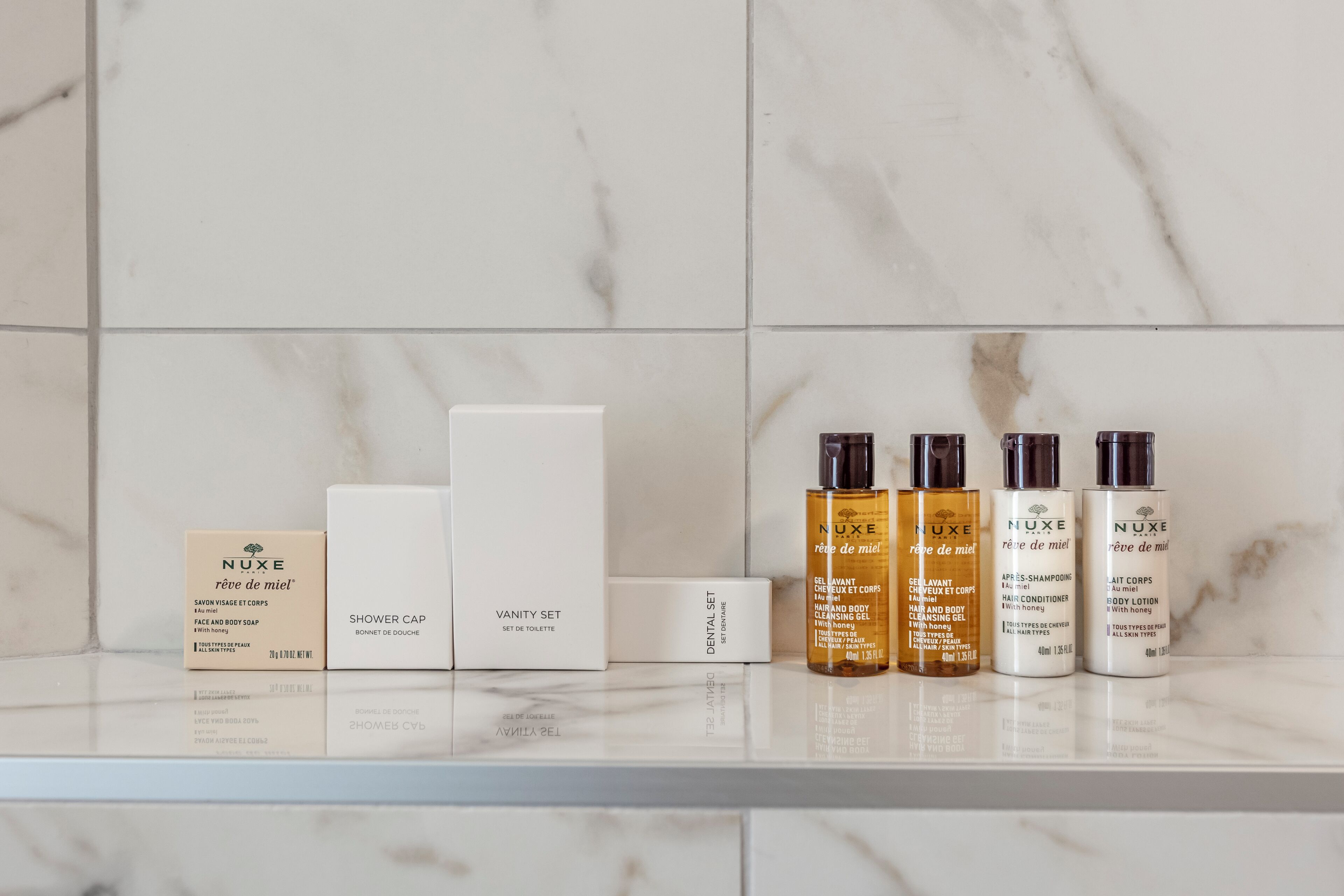 A bathroom shelf with various Nuxe skincare products, including a shower cap, a vanity set, and hair and body care items.