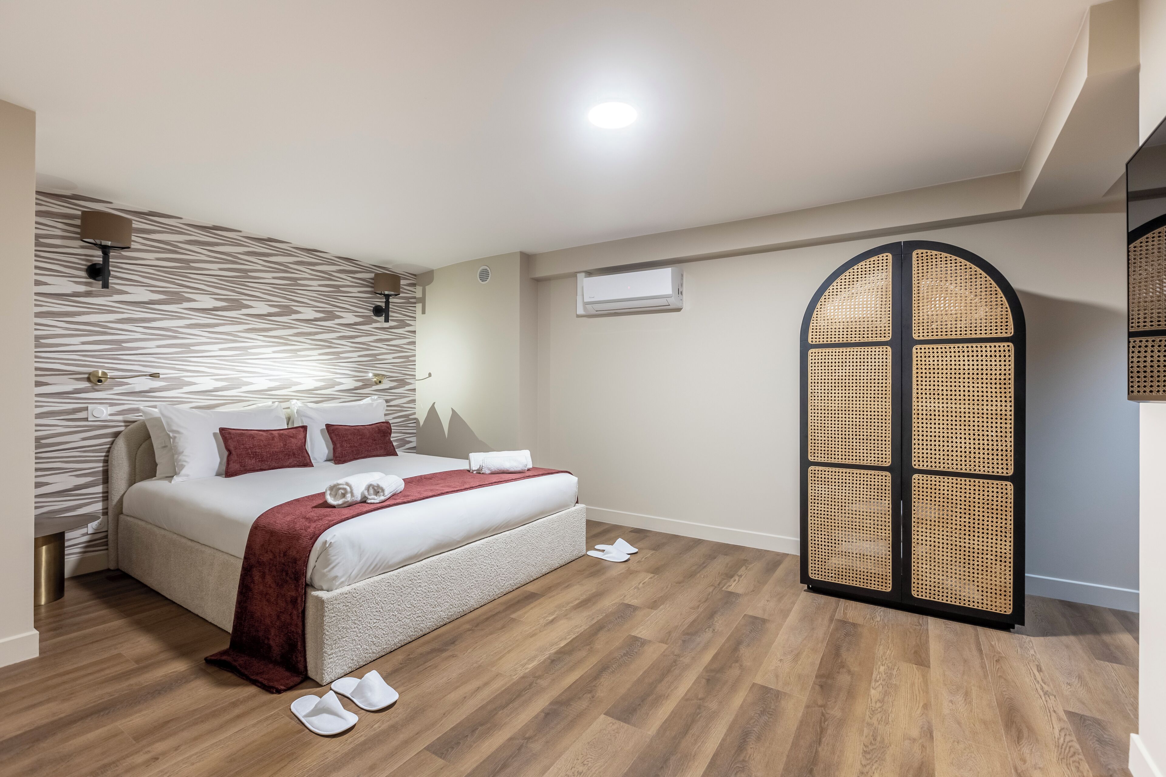 A bedroom with a bed, a bedside table, a wall-mounted air conditioner, and a woven partition.