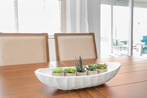 Uma mesa de jantar com um centro decorativo branco e texturizado, contendo várias pequenas plantas em vasos.
