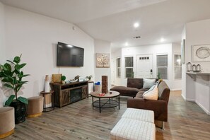 Uma sala de estar moderna com televisão de tela plana, um sofá marrom, uma mesa de centro e um móvel para aparelhos eletrônicos de madeira.