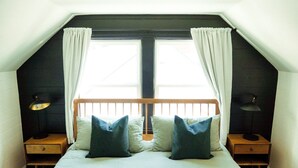 A bedroom with a sloped ceiling, a wooden headboard, two bedside tables with lamps, and a large window with curtains. - Cozy, Comfortable Home Base in Laurelhurst, Portland (Portland)