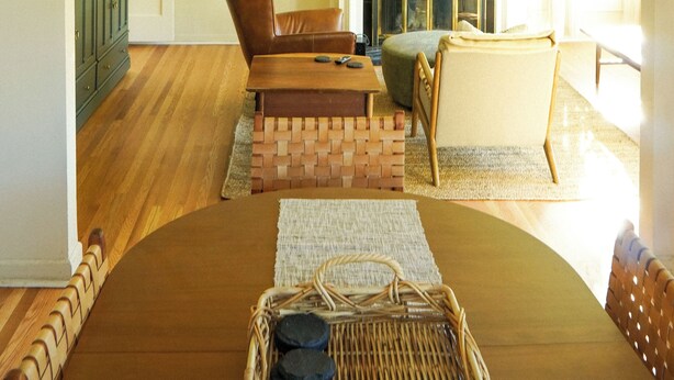 A living room with a chandelier, a fireplace, a brown sofa, a wicker basket, and a wooden floor. - Cozy, Comfortable Home Base in Laurelhurst, Portland (Portland)