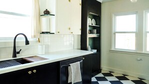 A kitchen with a black and white checkered floor, a white countertop, and a black cabinet with gold handles. - Cozy, Comfortable Home Base in Laurelhurst, Portland (Portland)