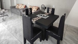 Een zithoek met een zwarte tafel en stoelen, een bank met gestreepte kussens en een kunstwerk in een lijst aan de muur.