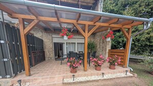 A covered patio area with outdoor seating, potted plants, and a stone wall.
