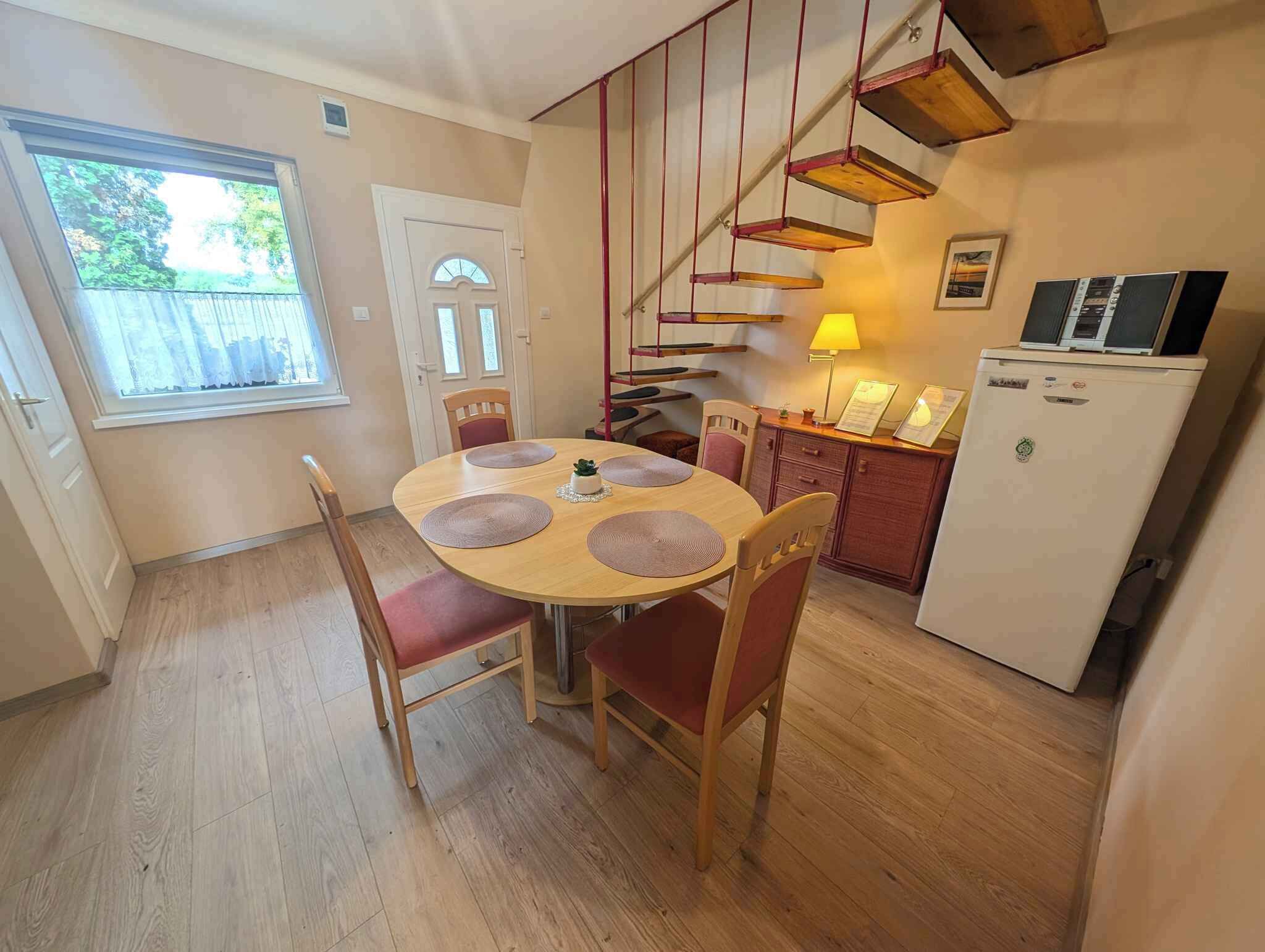 A dining area with a round table, four chairs, a small potted plant, and a staircase with wooden steps.