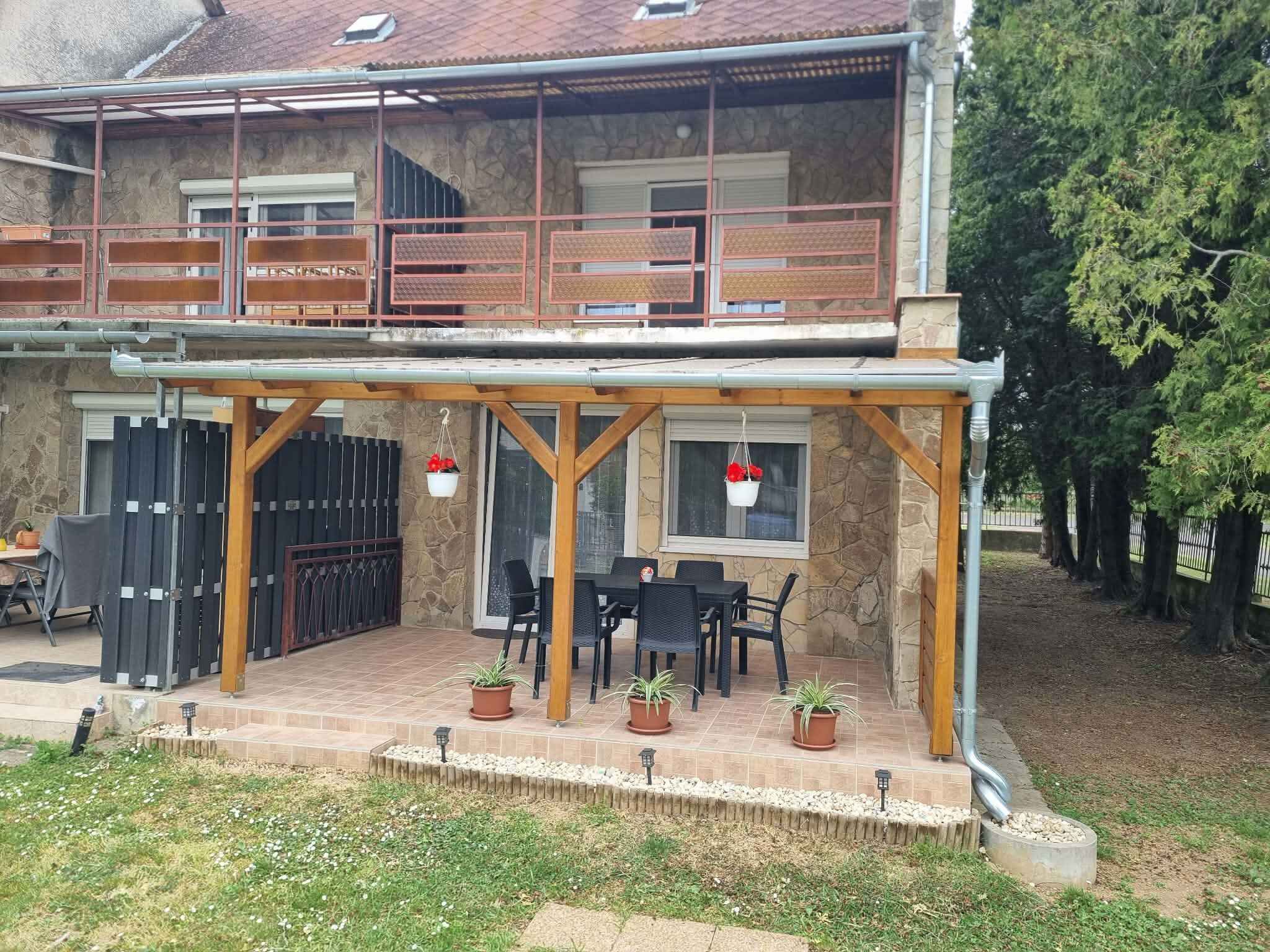Een tweelaags huis met een overdekte patio, buitenmeubels en potplanten.