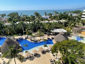 Um resort com uma piscina grande, palmeiras e vista para o oceano.