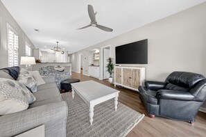Una sala de estar con sofá, mesa de centro y sillón de cuero, televisor de pantalla plana y ventilador de techo.