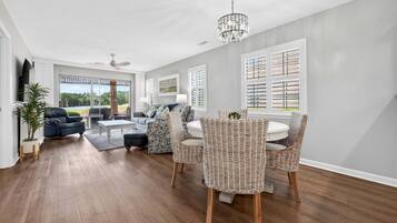 A spacious living room with a sofa, chairs, a coffee table, and a dining area with wicker chairs.