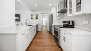A modern kitchen with white cabinetry, a central island, stainless steel appliances, and a herringbone tile backsplash. - 633 Managed by Brampton Park (Boynton Beach)