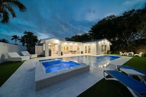 A modern house with a swimming pool, outdoor seating, and a well-lit patio area.
