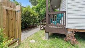 Una terraza de madera con una silla, un sendero que lleva a una casa y una valla de madera.