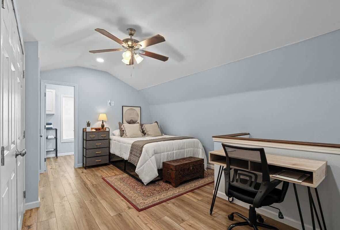 A bedroom with a bed, desk, chair, and a ceiling fan.