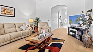 Un salon avec un canapé beige, une table basse, une lampe, une plante et un téléviseur.