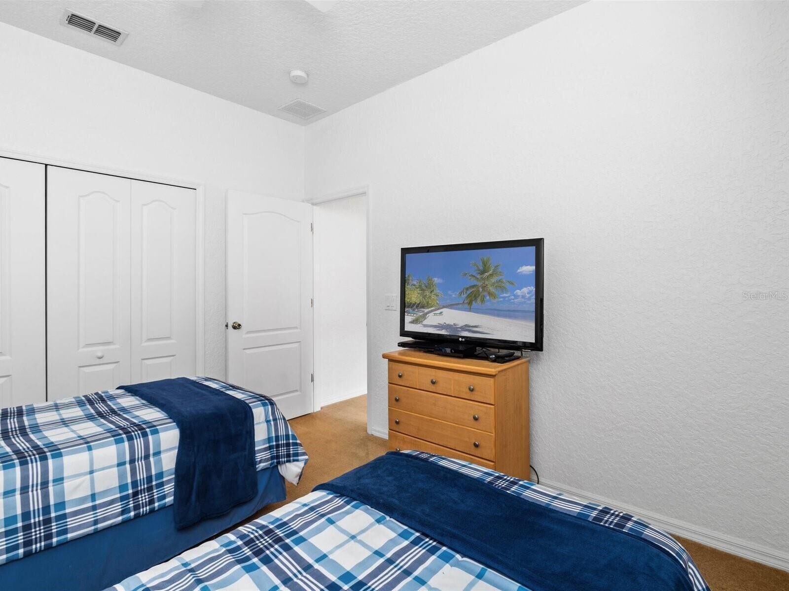 Quarto com duas camas, uma TV sobre um aparador de madeira e paredes brancas.