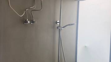 A bathroom with a shower, a handheld showerhead, and a wall-mounted faucet.