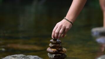 A hand balancing stones on a rock by a calm water body.