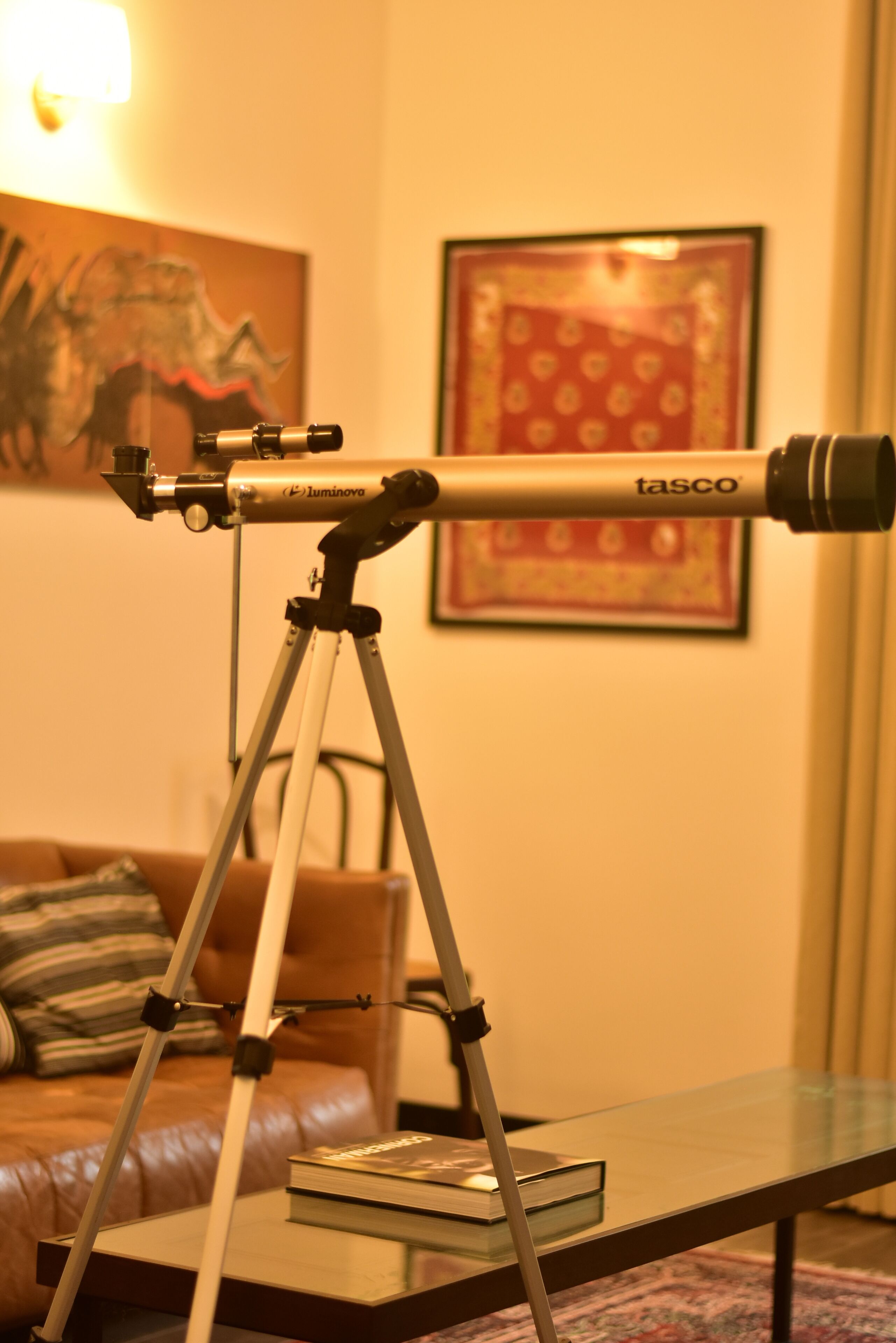 Een telescoop op een statief in een kamer met een bank en een ingelijst kunstwerk aan de muur.