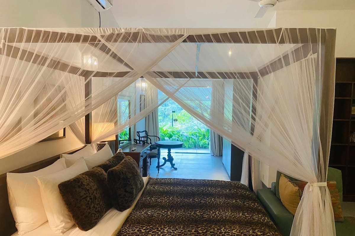 Une chambre avec un lit à baldaquin, une vue sur l’extérieur et un coin repas.