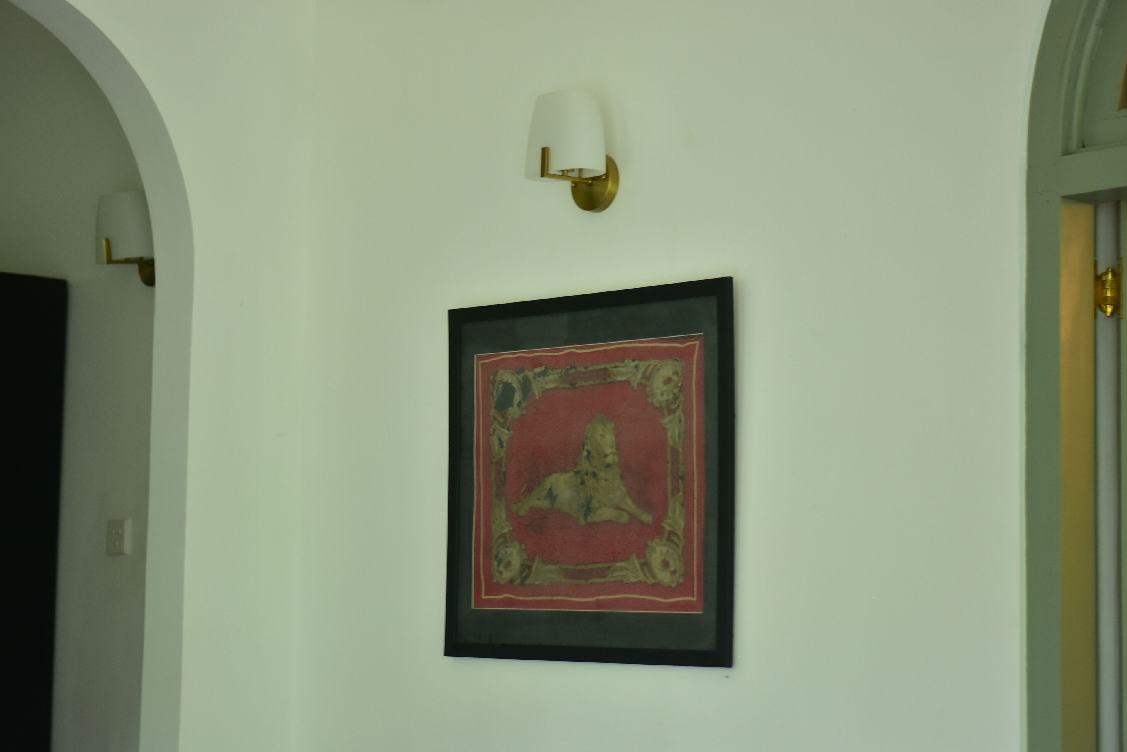 A hallway with a framed artwork on the wall and a wall-mounted light fixture.