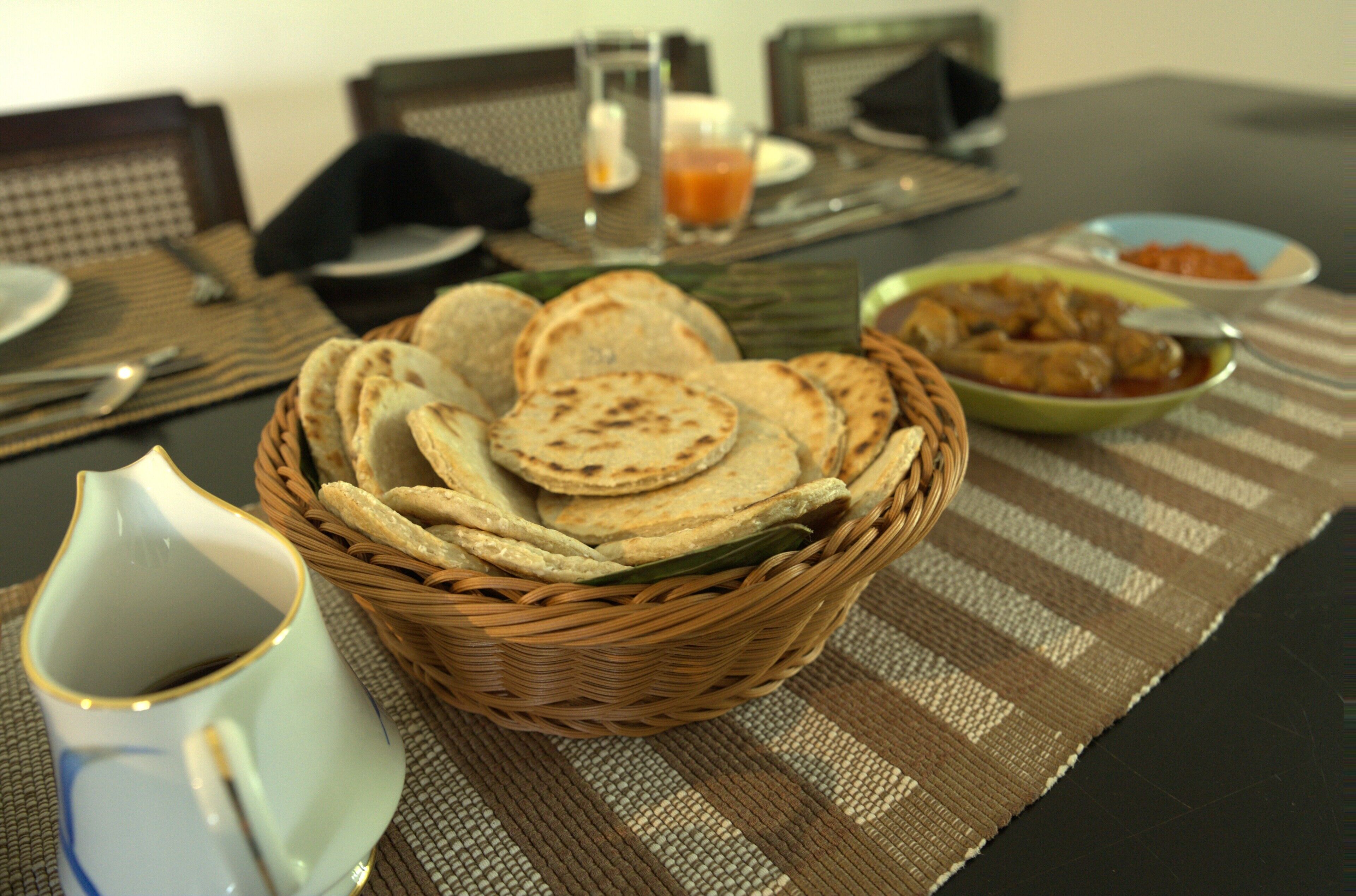 Una mesa con una cesta de panes planos, un plato de pollo y una taza de té.
