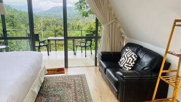 Un dormitorio con una cama grande, un sofá de cuero negro, una escalera de madera y vistas a exuberante vegetación.