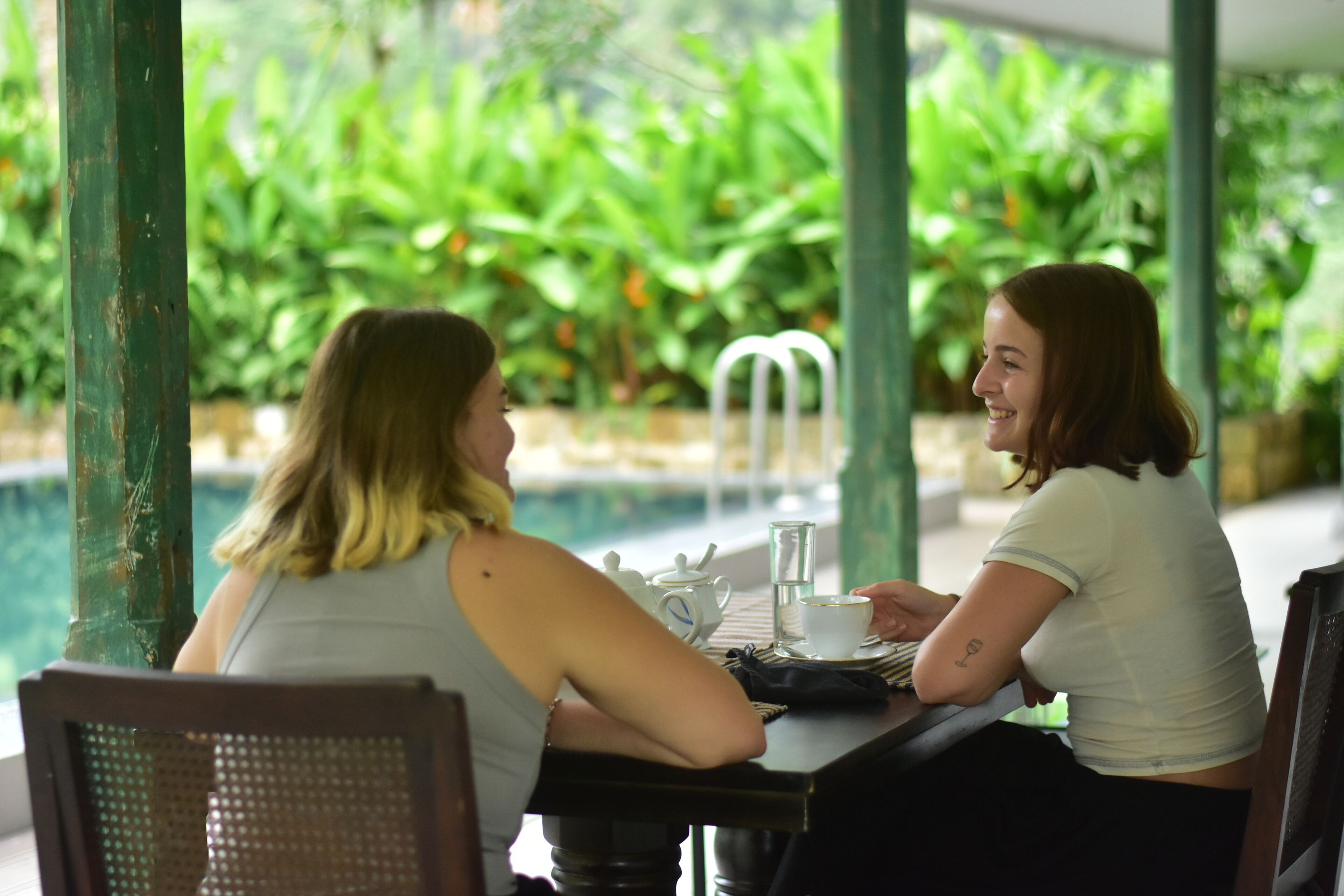 Two people sitting at a table with a teapot, cup, and saucer.