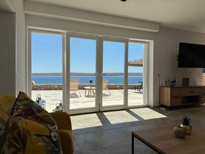 A living room with a large sliding glass door leading to a patio with a view of the sea. - Holiday home right by the sea (Lukovo Šugarje)
