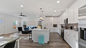 Una cocina moderna con armarios blancos, una isla central y un comedor con mesa y sillas.
