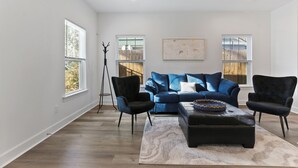 Una sala de estar moderna con un sofá azul, dos sillones negros, una mesa de centro y una lámpara de pie.