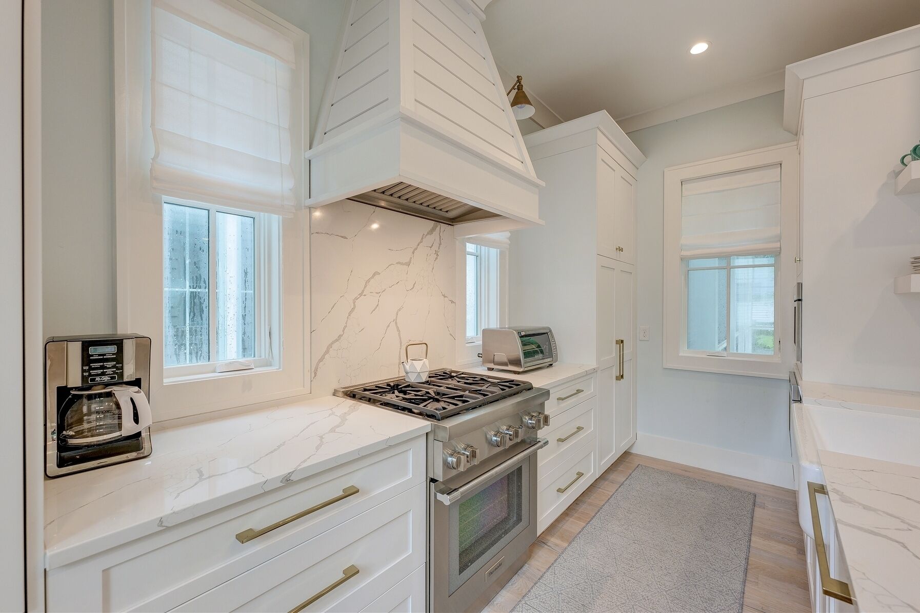 A modern kitchen with white cabinetry, a built-in stove, oven, and a coffee maker.