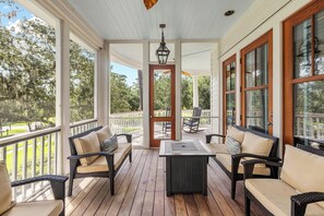 A covered porch with wicker furniture and a central table, overlooking a landscaped area. - Gem in Wilson Village with Private Pool, Game Room, and Bikes (Bluffton)
