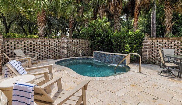 Un espace piscine avec des chaises longues, un jacuzzi et un mur de briques agrémenté de plantes grimpantes.