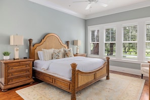 A bedroom with a wooden four-poster bed, a nightstand with a lamp, a dresser, and a window with blinds.