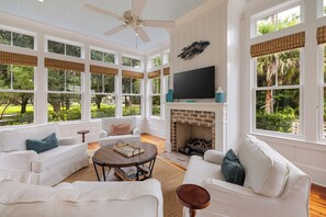A spacious living room with a fireplace, large windows, and a ceiling fan. - Gem in Wilson Village with Private Pool, Game Room, and Bikes (Bluffton)