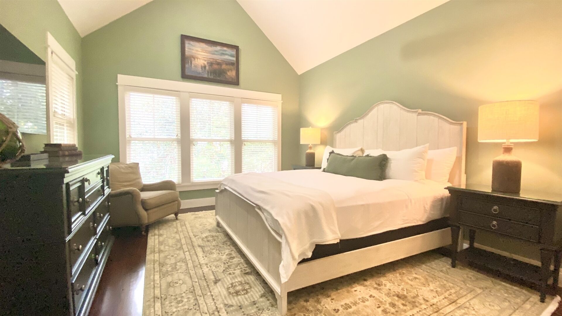 A bedroom with a large bed, a dresser, a chair, and a window with blinds.