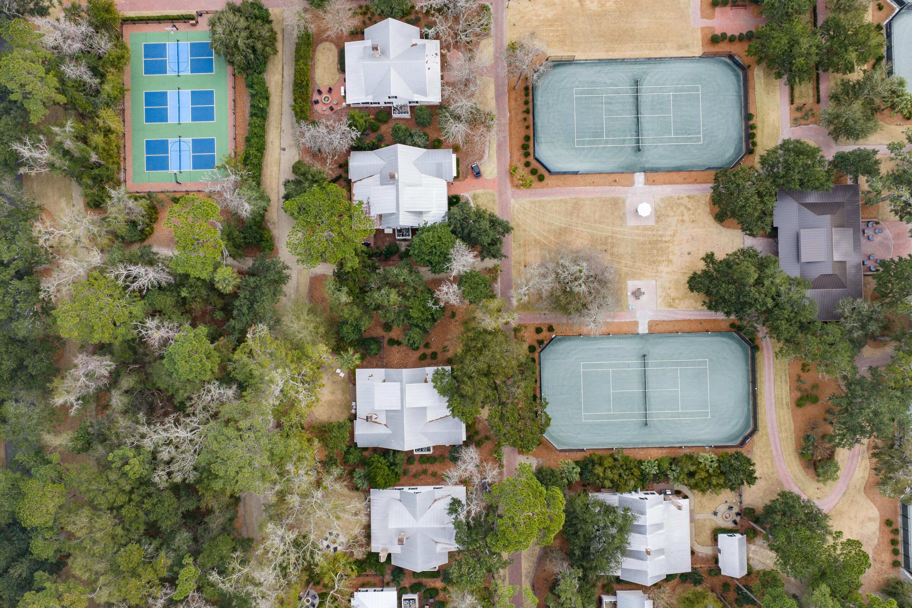An aerial view of a residential area with multiple houses, tennis courts, and surrounding greenery.