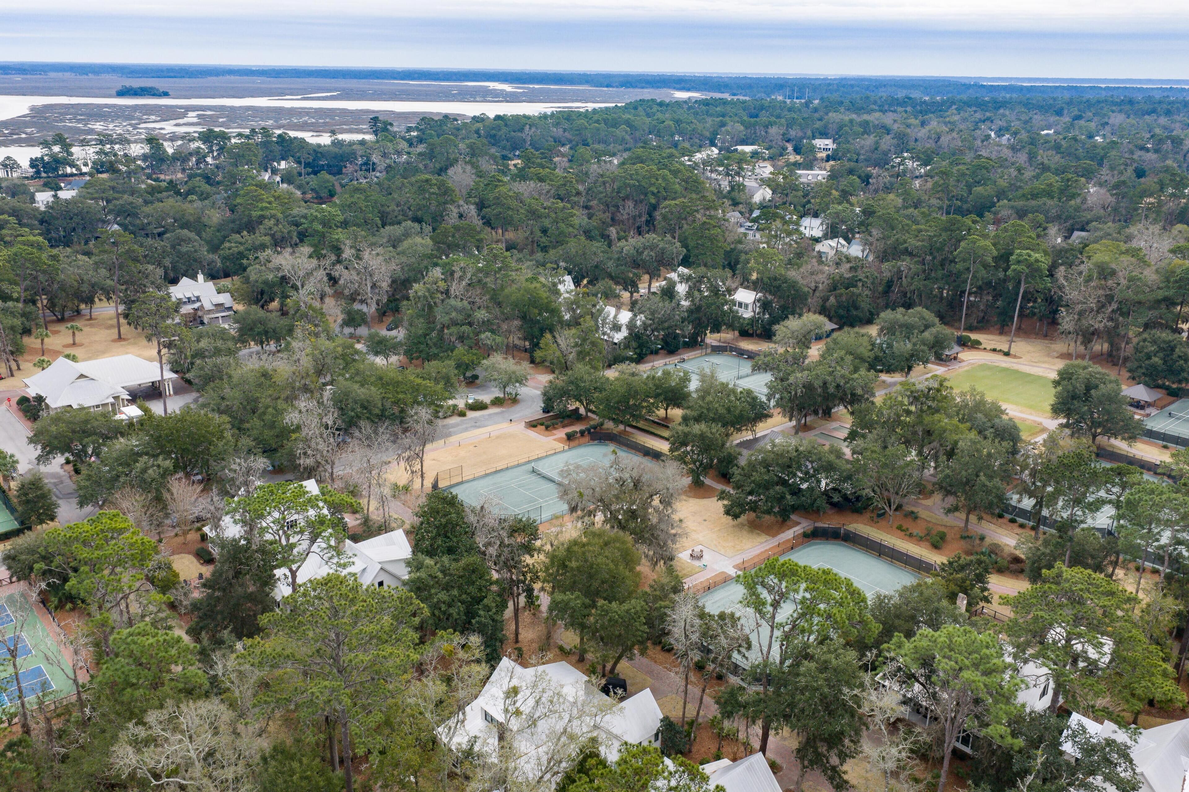 Vista aérea de una zona residencial con varias casas, una cancha de tenis y una gran masa de agua al fondo.