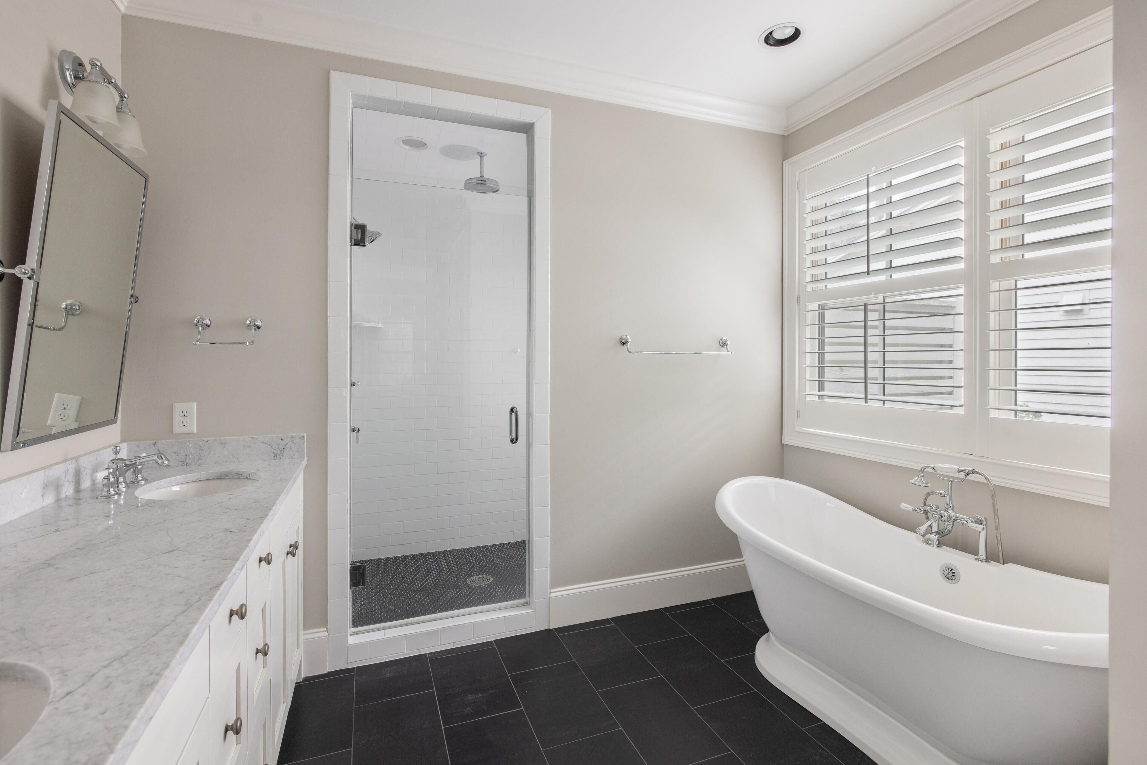 A bathroom with a shower, a bathtub, a sink, and a window with blinds.