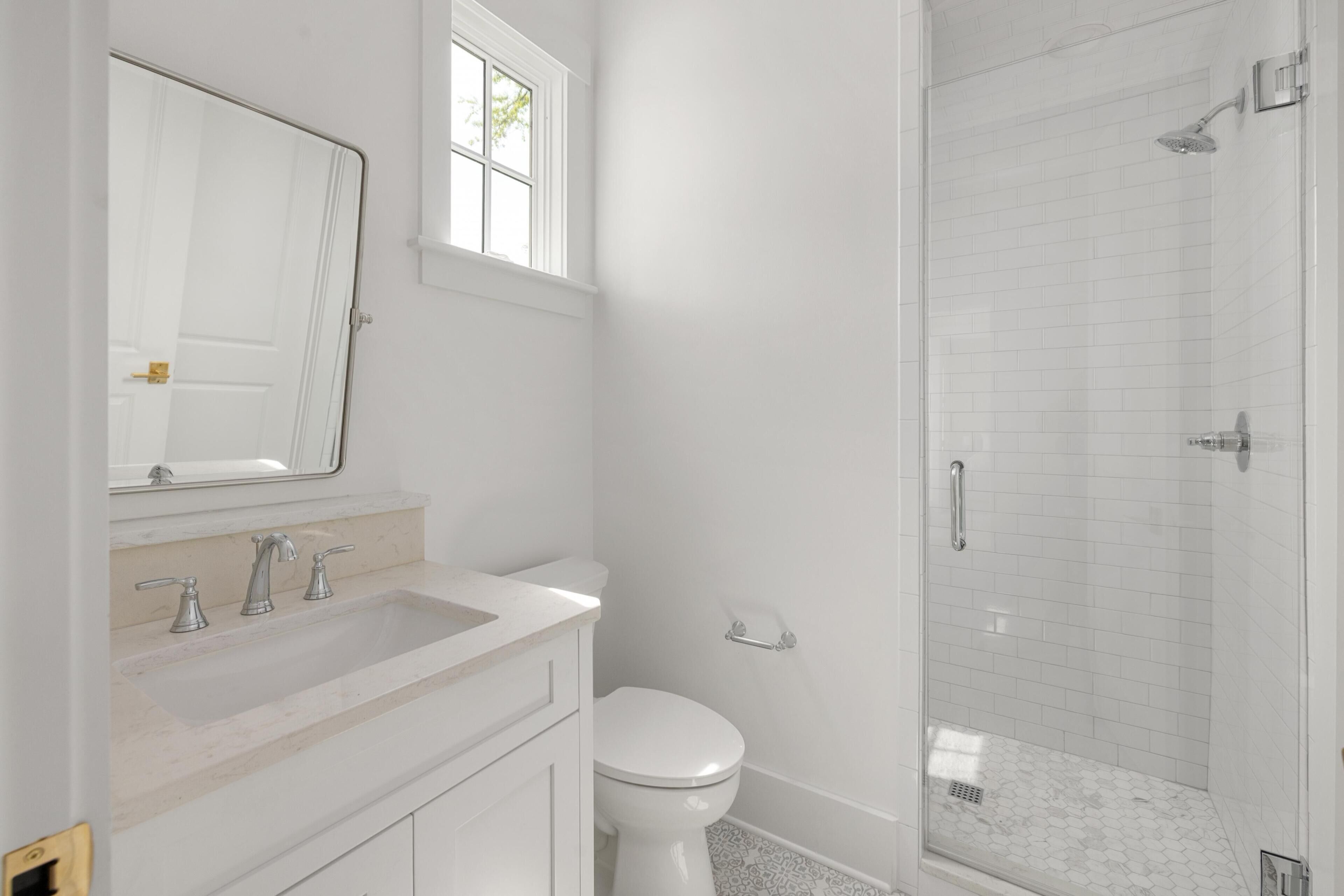 A bathroom with a white sink, mirror, toilet, and a glass-enclosed shower.