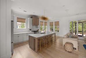 A modern kitchen with a central island, bar stools, and a dining area with a sofa. - Screened Porch, Bunk Room & Close to Moreland Amenities (Bluffton)