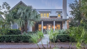 A two-story house with a porch, surrounded by palm trees and shrubs. - Cozy Fireplace on the Porch + Bunk Room, Close to Moreland Treehouse (Bluffton)