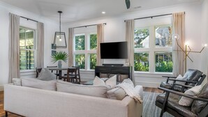 A modern living room with a sofa, a coffee table, a TV, and a dining area. - Cozy Fireplace on the Porch + Bunk Room, Close to Moreland Treehouse (Bluffton)