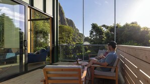 A wooden deck with a glass wall, a blue sofa, and a table with a laptop. - Trails End (Punakaiki)