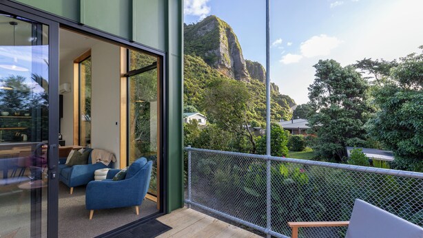 A balcony with a view of a mountain, a seating area with a sofa and chairs, and a glass door leading to a room. - Trails End (Punakaiki)