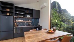 A modern kitchen with dark cabinetry, a wooden dining table, and a view of a mountainous landscape. - Trails End (Punakaiki)