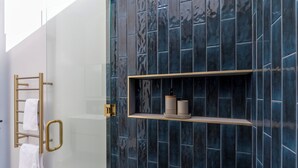 A bathroom with a glass door, a towel rack, and a shelf with two cylindrical containers. - Trails End (Punakaiki)